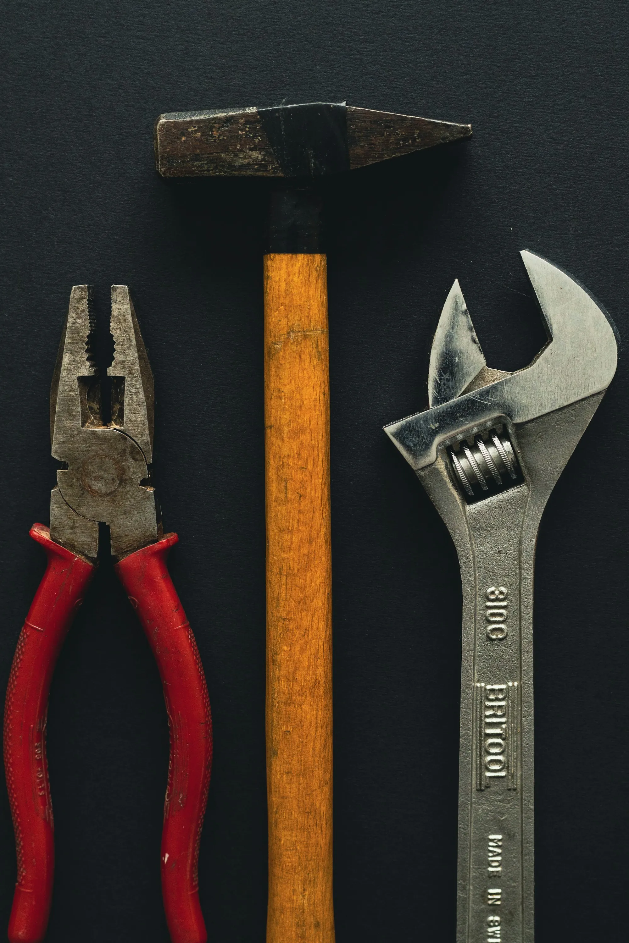 Red pliers and an adjustable wrench on a dark surface