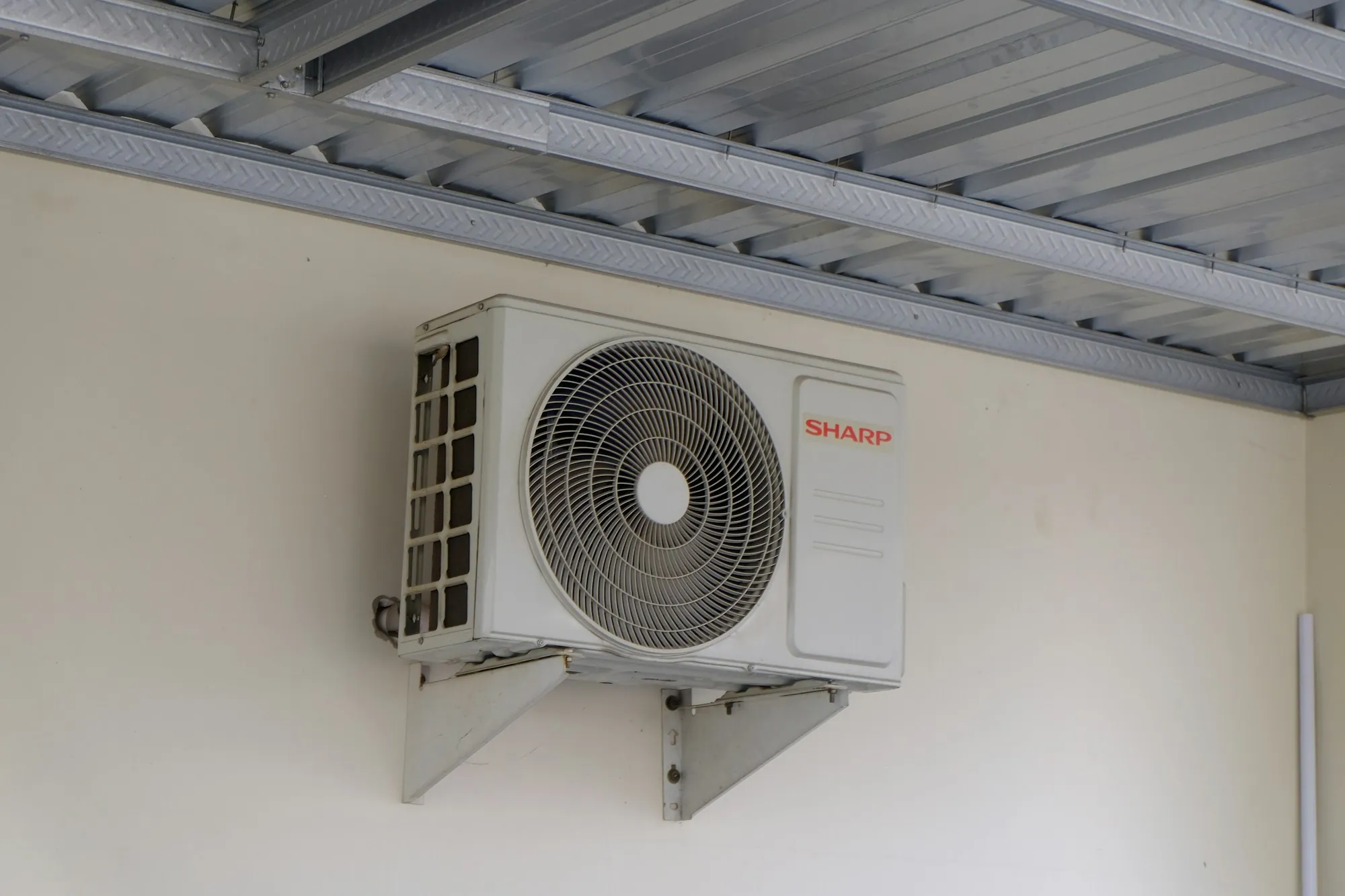 Wall-mounted air conditioner condenser under a covered eave