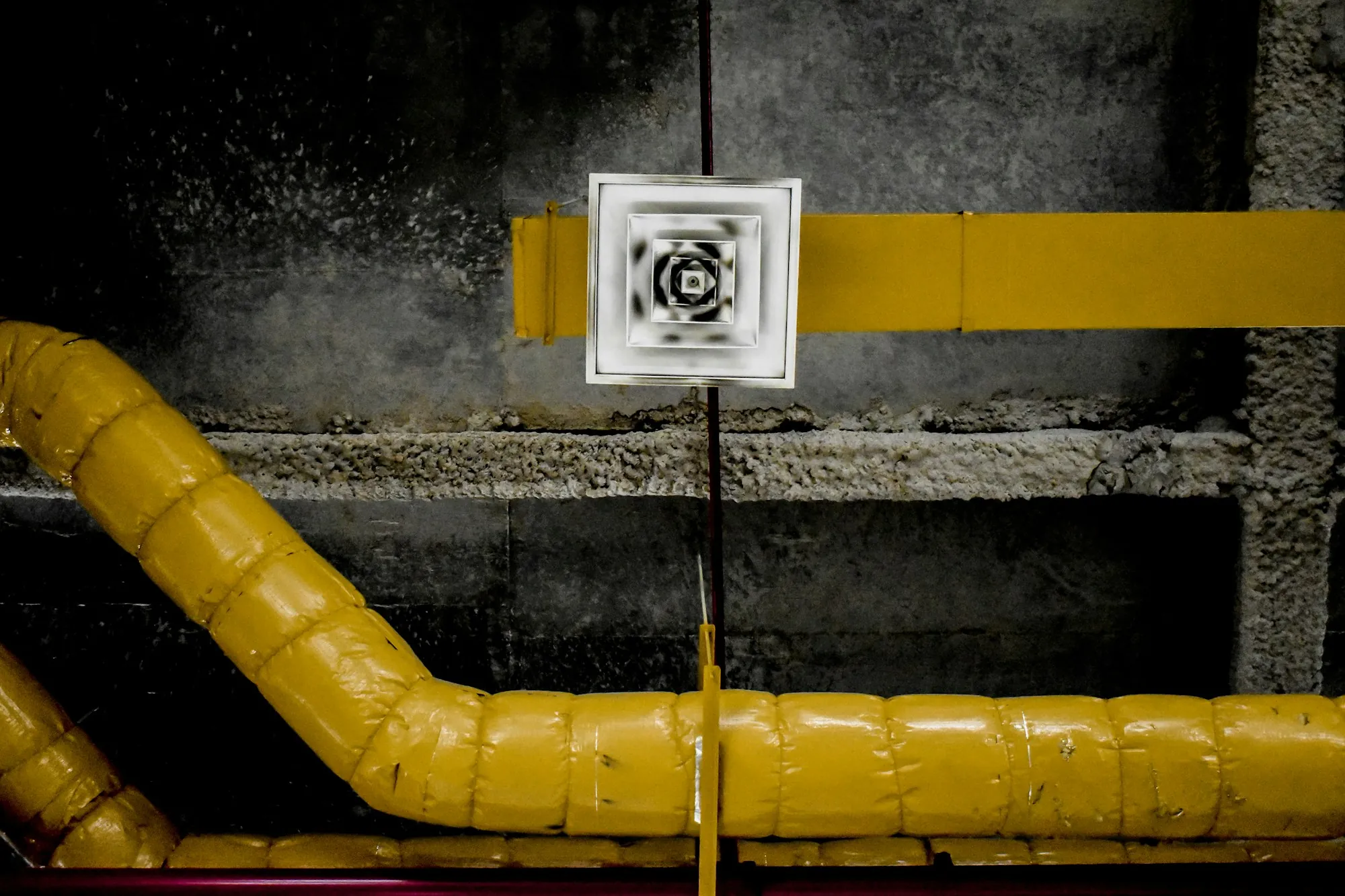 Square ceiling diffuser above exposed pipes
